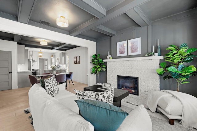 living room featuring light wood finished floors, coffered ceiling, visible vents, and a brick fireplace