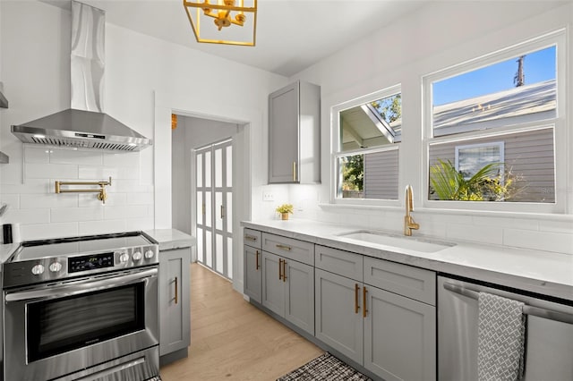 kitchen with light wood-style floors, stainless steel appliances, gray cabinetry, wall chimney range hood, and a sink