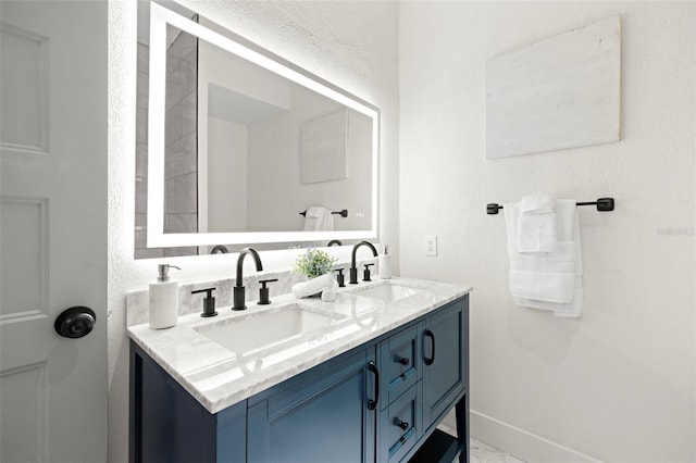 bathroom with marble finish floor, double vanity, a sink, and baseboards