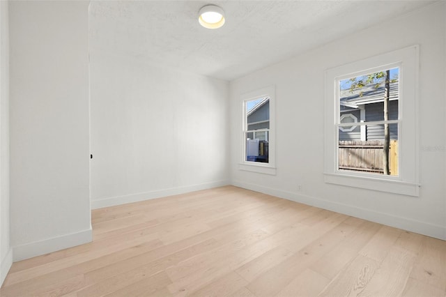 unfurnished room with light wood-type flooring, baseboards, and a textured ceiling