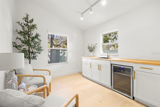 bar with lofted ceiling, wine cooler, a sink, light wood-type flooring, and a wealth of natural light