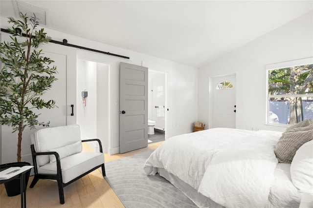 bedroom with a barn door, visible vents, ensuite bathroom, vaulted ceiling, and light wood-style floors