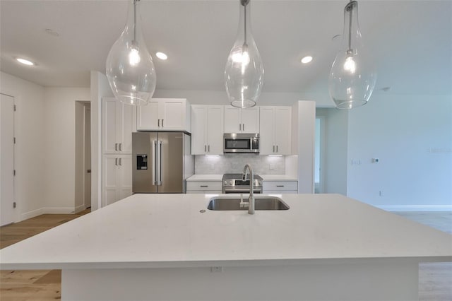 kitchen with decorative backsplash, an island with sink, stainless steel appliances, white cabinetry, and a sink