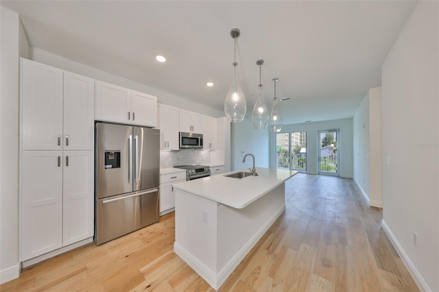 kitchen featuring a center island with sink, decorative backsplash, stainless steel appliances, white cabinetry, and a sink