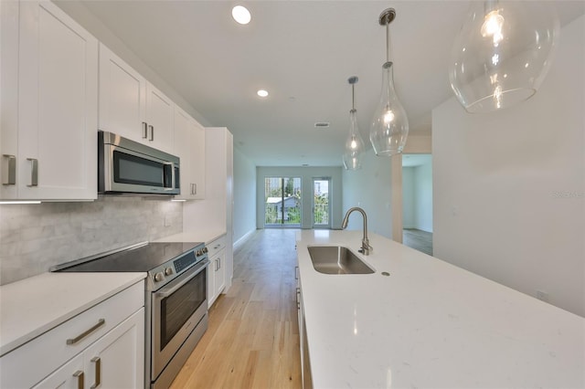 kitchen with stainless steel appliances, backsplash, light wood-style flooring, white cabinetry, and a sink