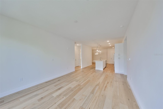 unfurnished living room featuring an inviting chandelier, a sink, light wood-style flooring, and baseboards