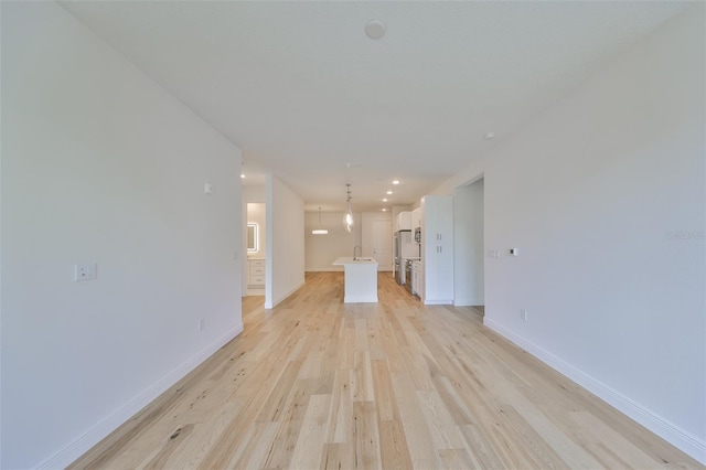 unfurnished living room with light wood finished floors, baseboards, and a sink