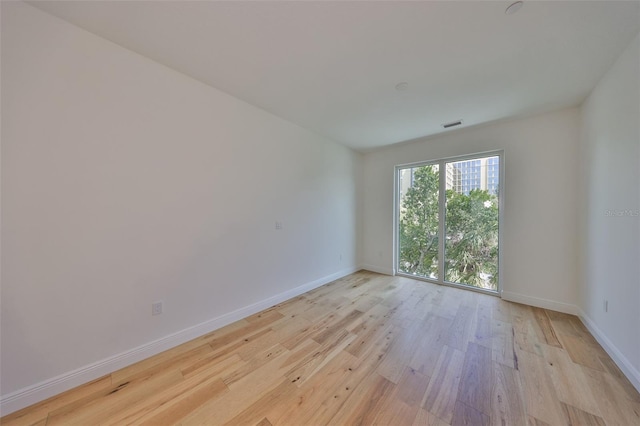 unfurnished room with light wood finished floors, visible vents, and baseboards