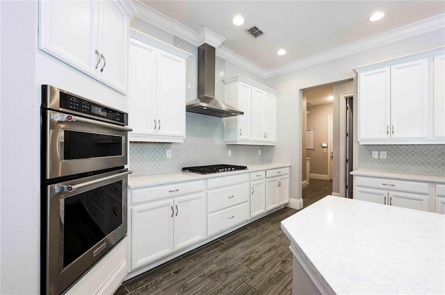 kitchen featuring double oven, gas cooktop, white cabinets, light countertops, and wall chimney range hood