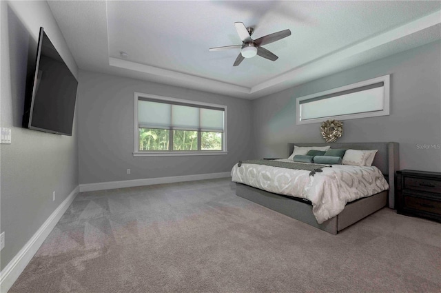 bedroom with a tray ceiling, carpet flooring, ceiling fan, and baseboards