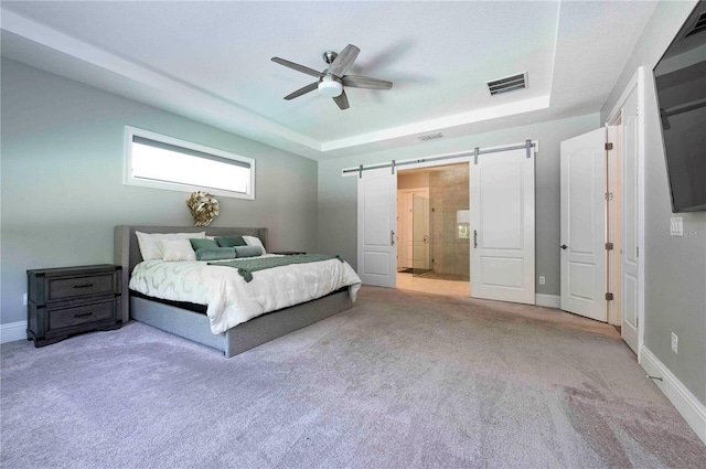 carpeted bedroom featuring a barn door, visible vents, a raised ceiling, and baseboards