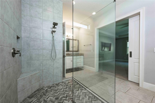 bathroom featuring a textured ceiling, vanity, baseboards, tiled shower, and tile patterned floors