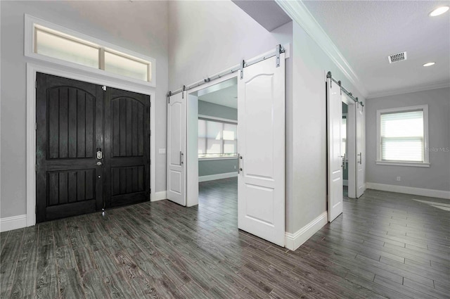 foyer entrance with wood finished floors, visible vents, crown molding, and a barn door