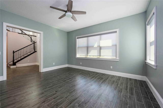 spare room with a ceiling fan, dark wood-style flooring, baseboards, and stairs