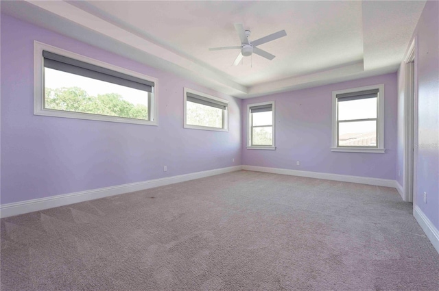 empty room with a raised ceiling, light carpet, ceiling fan, and baseboards