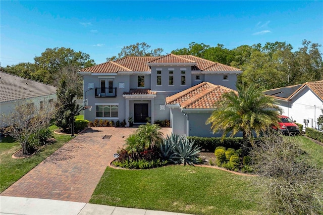 mediterranean / spanish-style house with a balcony, a tiled roof, decorative driveway, stucco siding, and a front yard