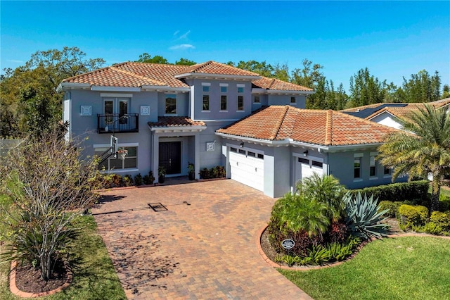 mediterranean / spanish-style house with a garage, decorative driveway, a tiled roof, and a balcony