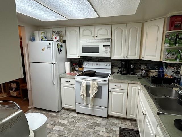 kitchen featuring white appliances, white cabinetry, and a sink