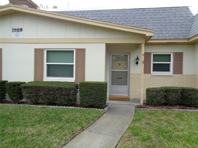 view of exterior entry featuring brick siding, a lawn, mansard roof, and roof with shingles