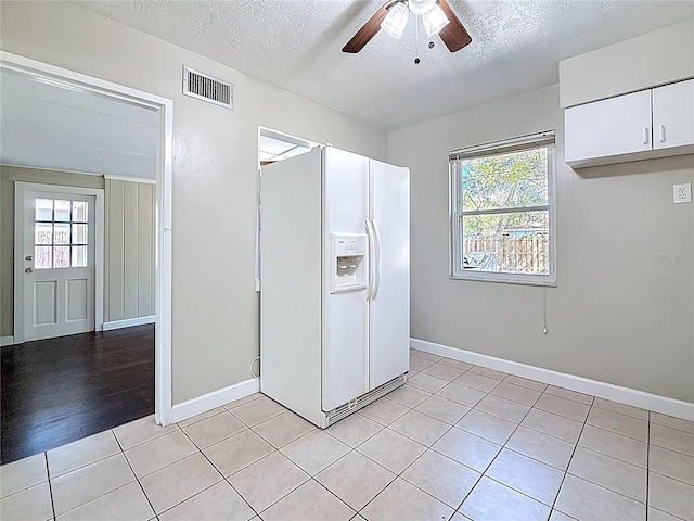 kitchen featuring plenty of natural light, white cabinetry, white fridge with ice dispenser, and visible vents