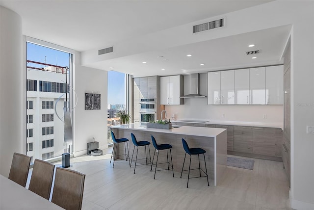 kitchen with black electric cooktop, visible vents, wall chimney exhaust hood, and modern cabinets