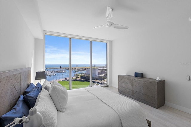 bedroom featuring expansive windows, a water view, a ceiling fan, and baseboards