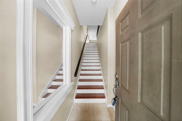 stairs featuring a textured ceiling, tile patterned flooring, and baseboards