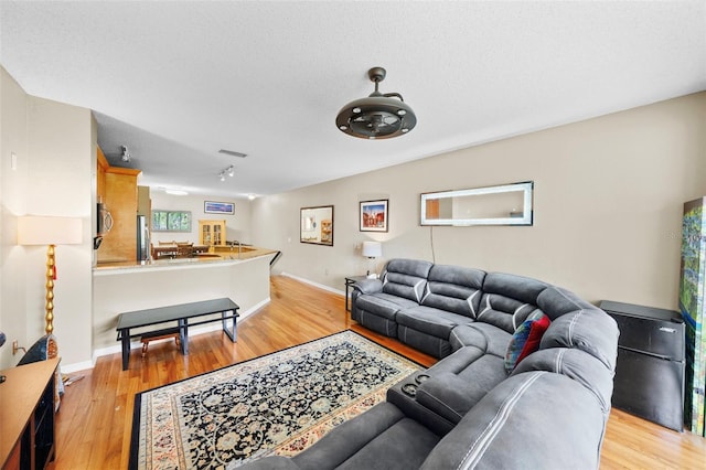 living area with light wood finished floors, baseboards, visible vents, and a textured ceiling