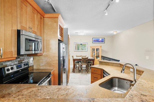 kitchen with decorative backsplash, light stone countertops, stainless steel appliances, a textured ceiling, and a sink