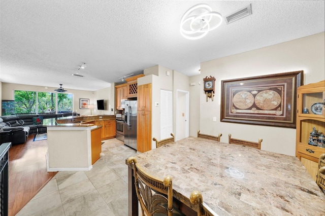 kitchen with open floor plan, visible vents, stainless steel refrigerator with ice dispenser, and a textured ceiling