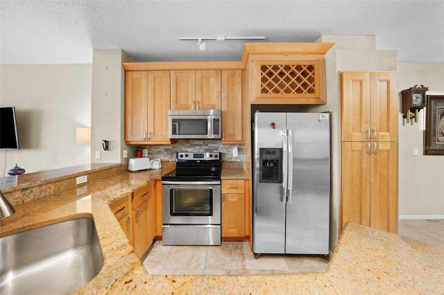 kitchen featuring tasteful backsplash, light stone countertops, stainless steel appliances, a textured ceiling, and a sink