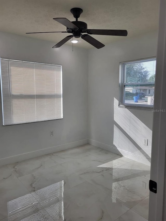 unfurnished room featuring baseboards, a textured ceiling, marble finish floor, and ceiling fan