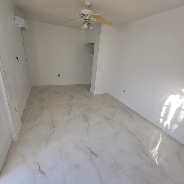 empty room with an AC wall unit, marble finish floor, and ceiling fan