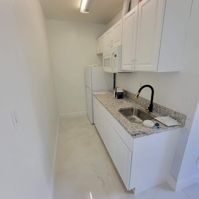 kitchen featuring a sink, white appliances, white cabinets, baseboards, and light stone countertops