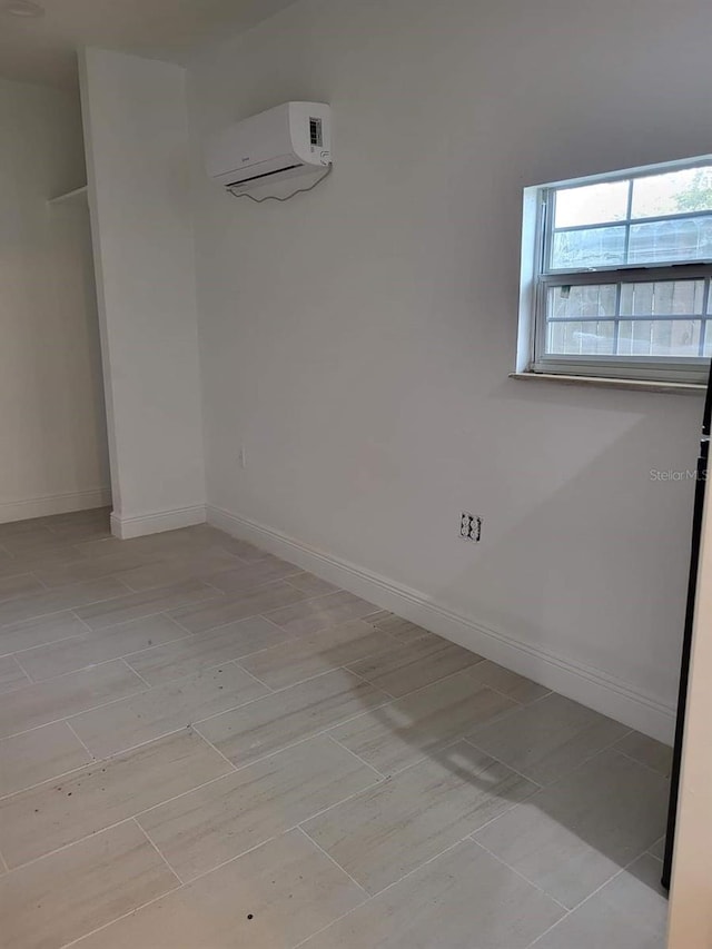 spare room with a wall unit AC, baseboards, and light wood-type flooring