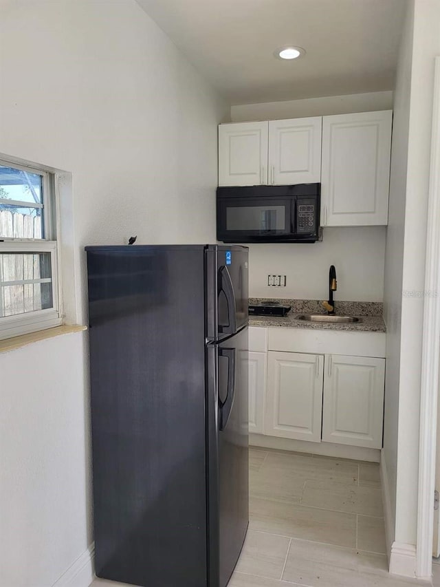 kitchen with light stone counters, white cabinets, black appliances, and a sink