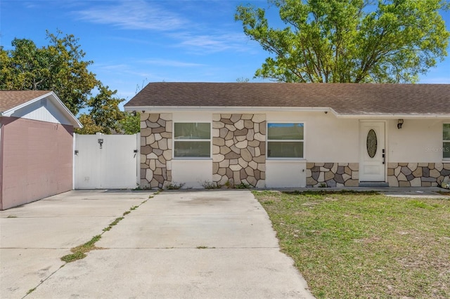 single story home featuring stucco siding, a front lawn, a gate, stone siding, and roof with shingles