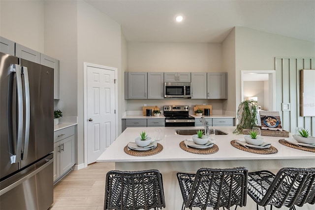 kitchen featuring a breakfast bar area, appliances with stainless steel finishes, gray cabinets, and a sink