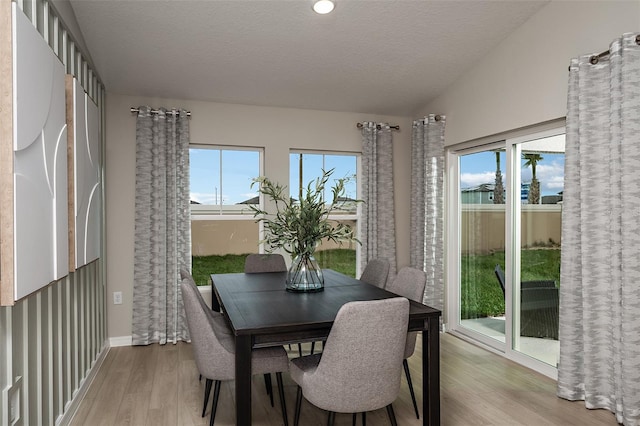 dining area with light wood-type flooring, baseboards, and a textured ceiling