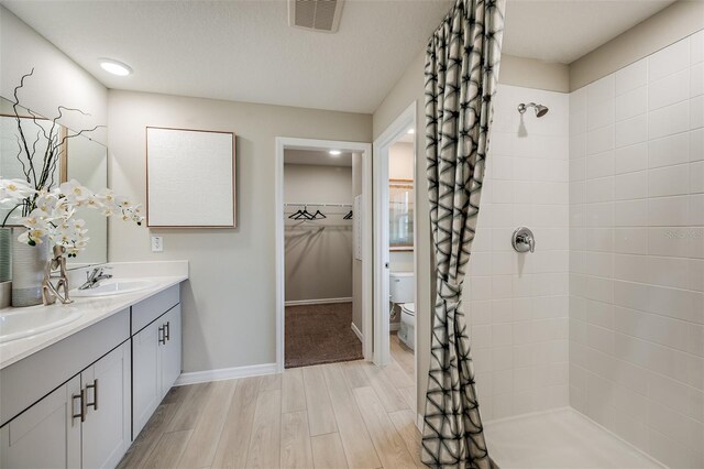 full bathroom with toilet, visible vents, a sink, and tiled shower