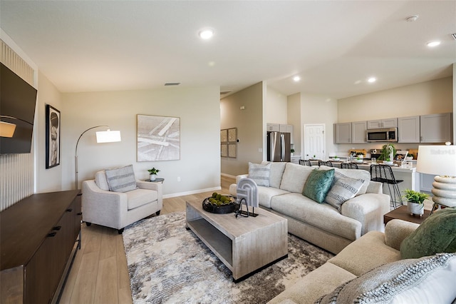 living area featuring lofted ceiling, recessed lighting, visible vents, light wood-style flooring, and baseboards