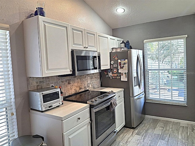 kitchen with a textured wall, stainless steel appliances, light wood-type flooring, and decorative backsplash