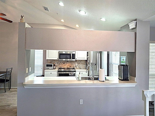 kitchen featuring a peninsula, tasteful backsplash, visible vents, and appliances with stainless steel finishes