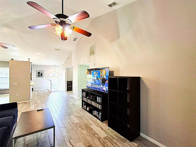 living area featuring high vaulted ceiling, light wood-style flooring, visible vents, and a ceiling fan