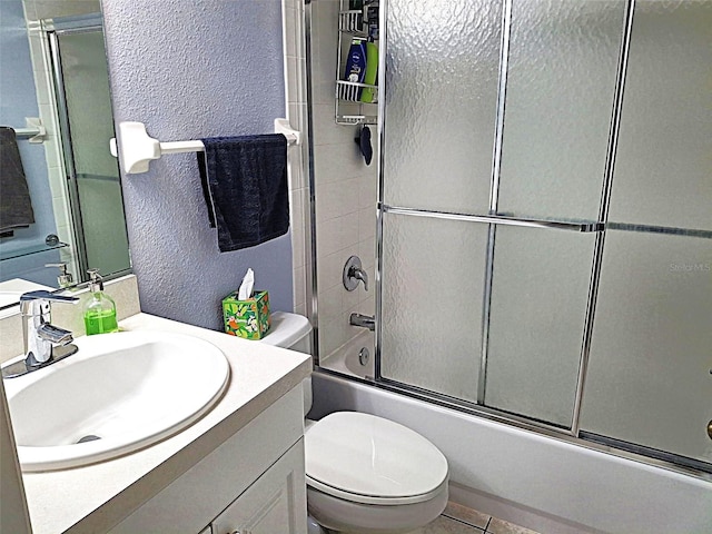 bathroom with a textured wall, toilet, enclosed tub / shower combo, tile patterned flooring, and vanity