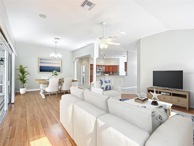 living area featuring visible vents, light wood-style flooring, ceiling fan with notable chandelier, decorative columns, and vaulted ceiling