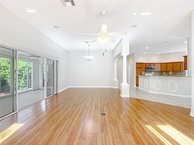 unfurnished living room with visible vents, ornate columns, baseboards, light wood-style floors, and ceiling fan with notable chandelier