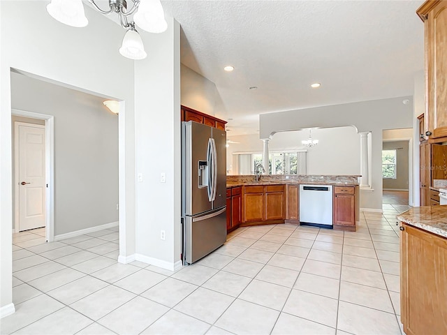 kitchen featuring light stone countertops, ornate columns, light tile patterned flooring, appliances with stainless steel finishes, and a notable chandelier