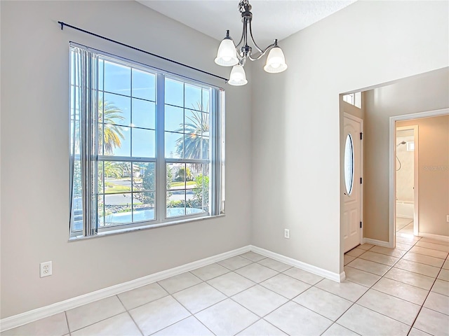 spare room with a notable chandelier, light tile patterned flooring, and baseboards