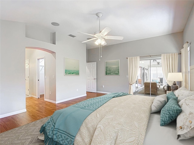 bedroom featuring visible vents, wood finished floors, baseboards, arched walkways, and lofted ceiling